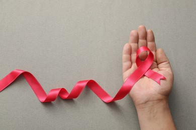 Photo of Man holding pink ribbon on grey background, top view with space for text. Breast cancer awareness concept