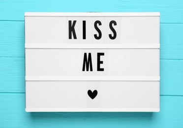 Photo of Light box with phrase Kiss Me on turquoise wooden background, top view