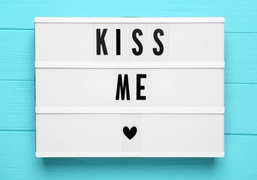 Light box with phrase Kiss Me on turquoise wooden background, top view