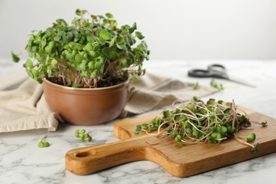 Photo of Bowl and board with fresh radish microgreens on white marble table