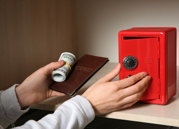 Photo of Woman putting passport and money into red steel safe, closeup