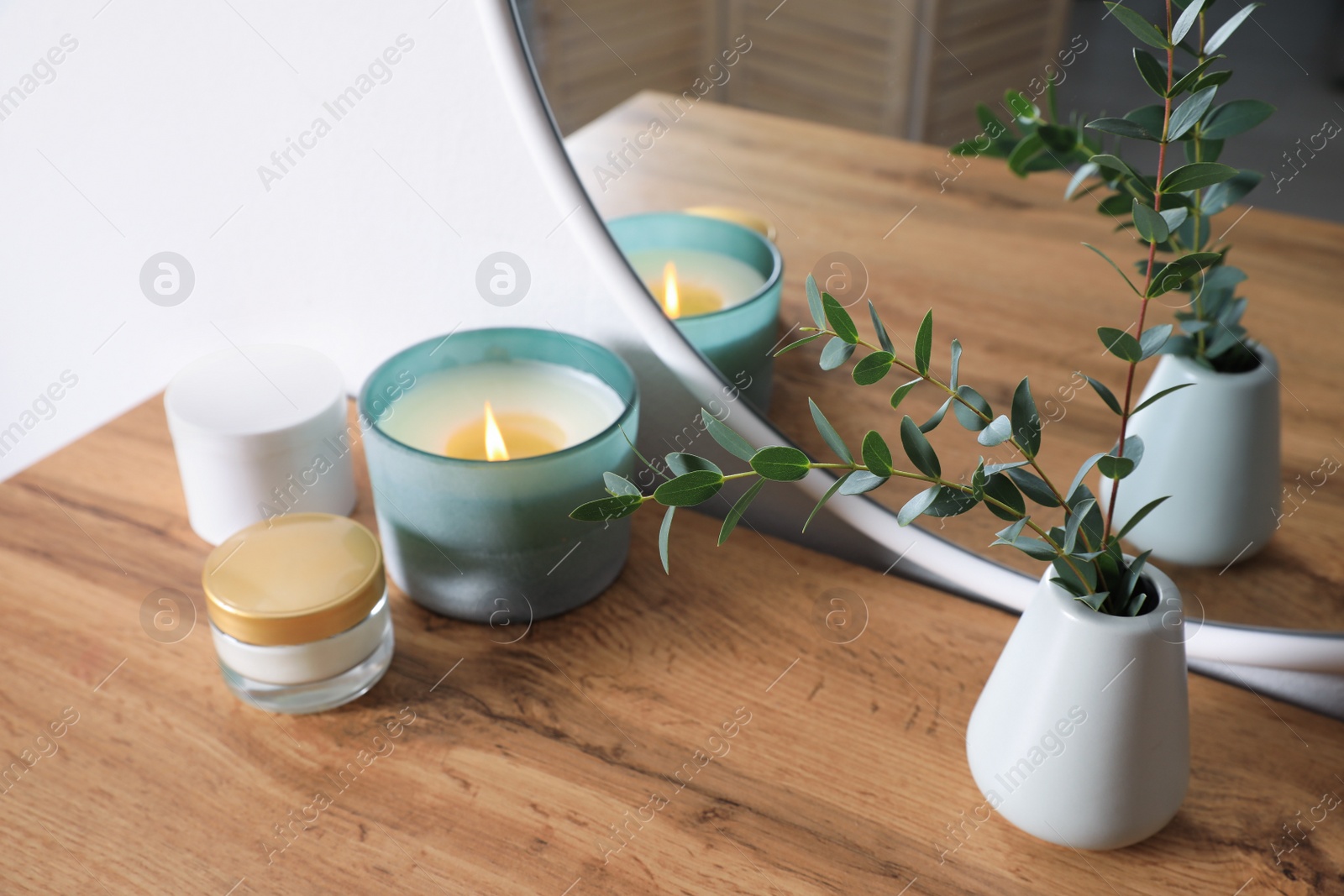 Photo of Burning candle, cosmetic products and vase on wooden dressing table
