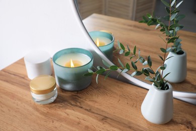 Burning candle, cosmetic products and vase on wooden dressing table