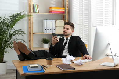 Lazy employee using smartphone while resting at table in office