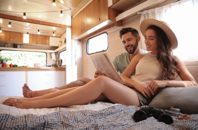 Happy young couple reading newspaper on bed in trailer. Camping vacation