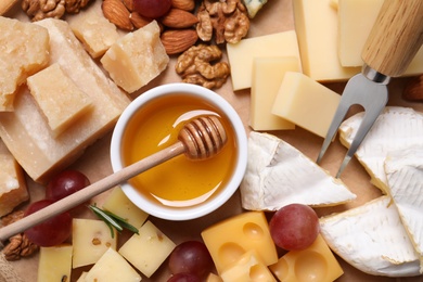 Photo of Cheese plate with honey, grapes and nuts on wooden board, top view