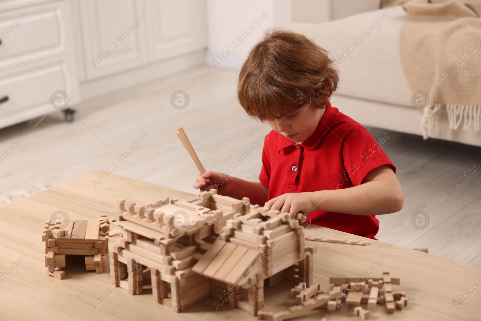 Photo of Cute little boy playing with wooden construction set at table in room. Child's toy