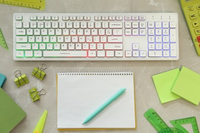 Modern keyboard with RGB lighting and stationery on grey marble table, flat lay