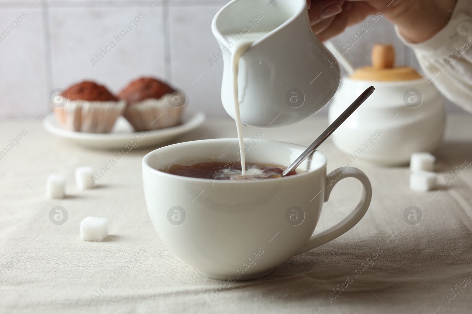 Photo of Pouring milk into cup with tea on light table, closeup