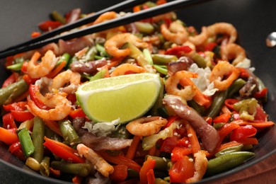 Photo of Shrimp stir fry with vegetables and chopsticks in wok, closeup