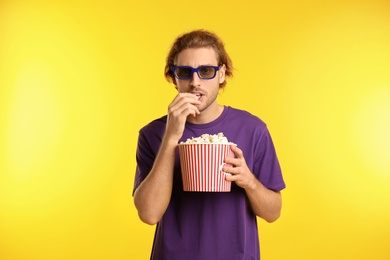 Man with 3D glasses and popcorn during cinema show on color background