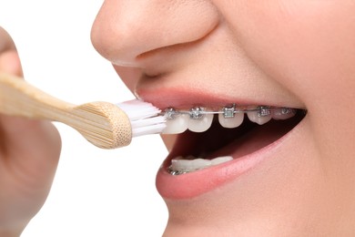 Woman with dental braces cleaning teeth on white background, closeup