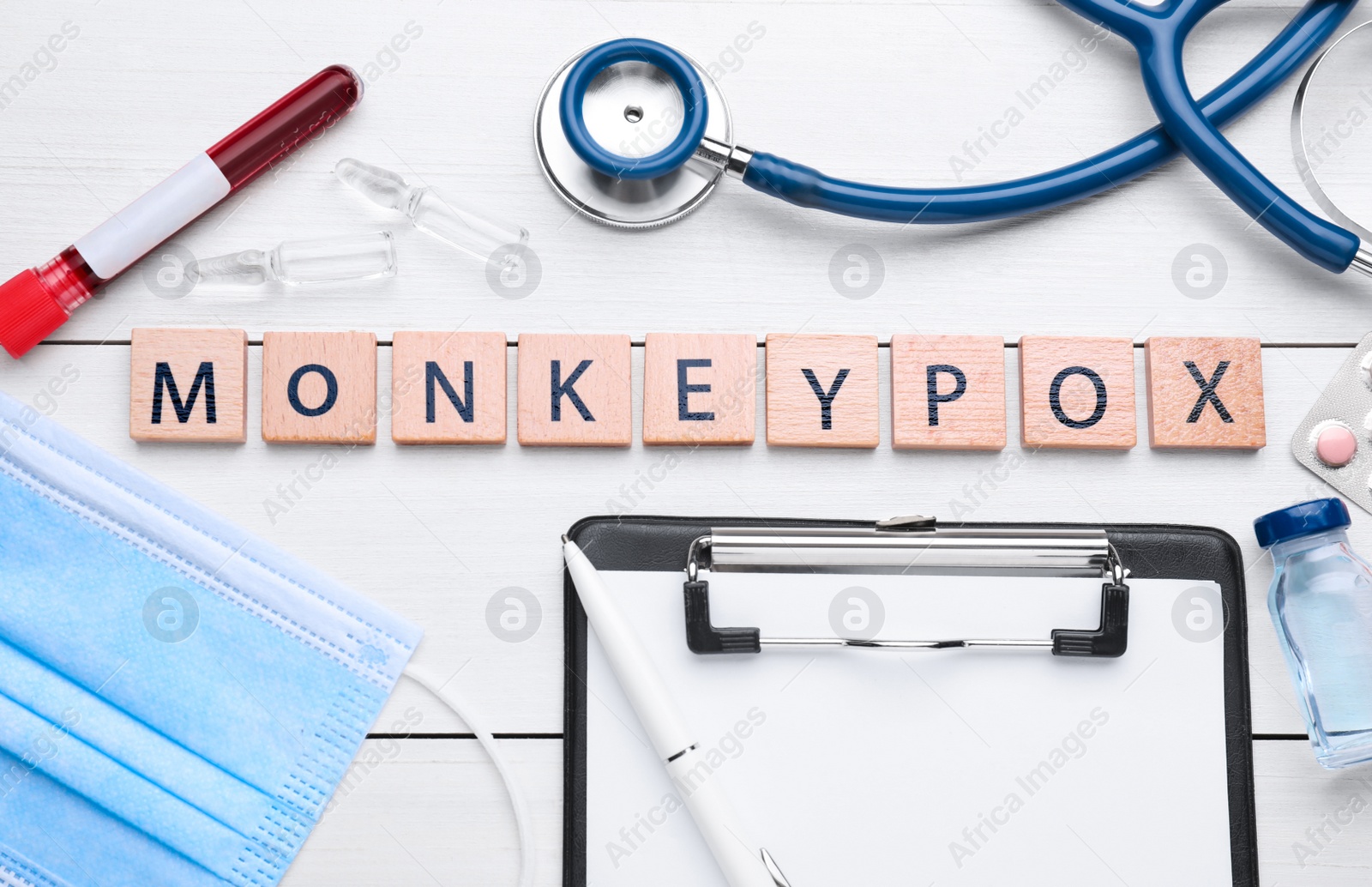 Photo of Flat lay composition with word Monkeypox made of squares and medical supplies on white wooden table