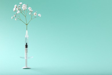 Photo of Cosmetology. Medical syringe and gypsophila on turquoise background, space for text