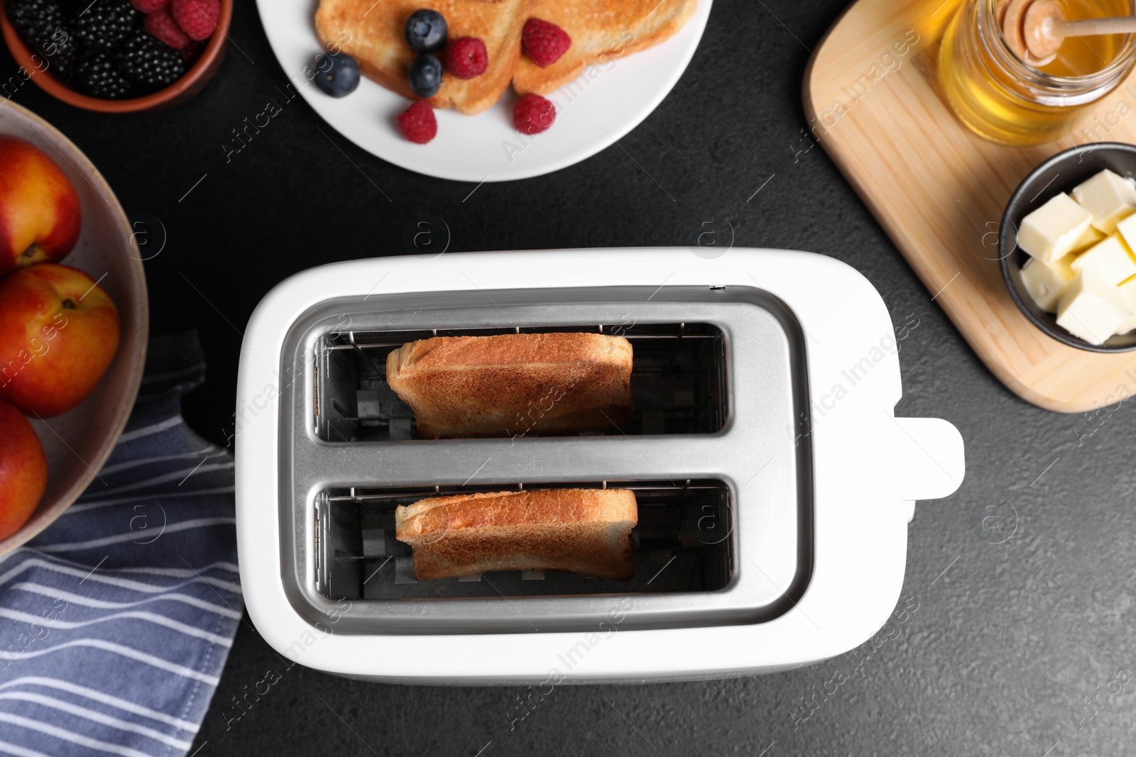 Photo of Modern toaster with slices of bread, honey and fresh berries on black table, flat lay