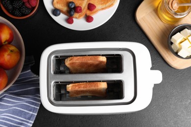 Modern toaster with slices of bread, honey and fresh berries on black table, flat lay