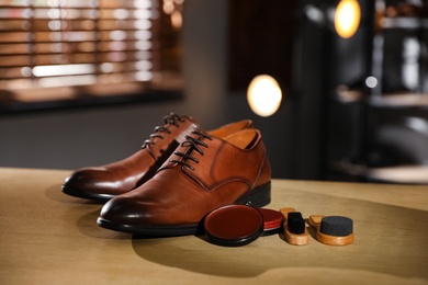 Pair of shoes and items for footwear care on wooden table in workshop