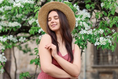 Beautiful woman in straw hat near blossoming tree on spring day