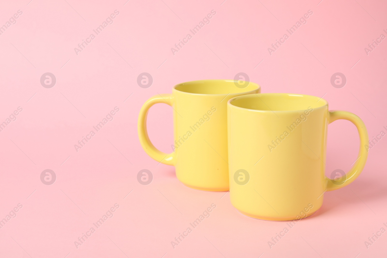 Photo of Two yellow ceramic mugs on pink background, space for text