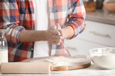 Man sprinkling flour over board on table in kitchen
