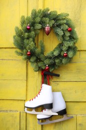 Pair of ice skates and Christmas wreath hanging on old yellow door