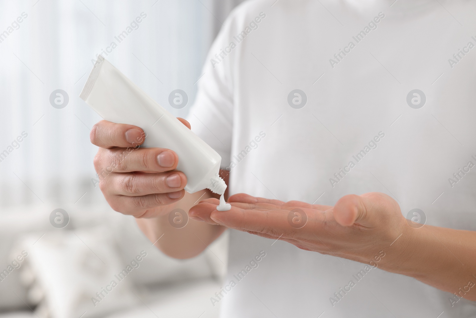 Photo of Man applying body cream onto his hand indoors, closeup