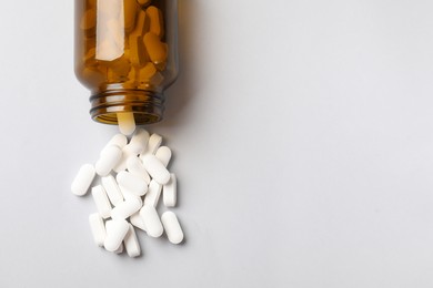 Photo of Vitamin pills and bottle on light grey background, top view. Space for text