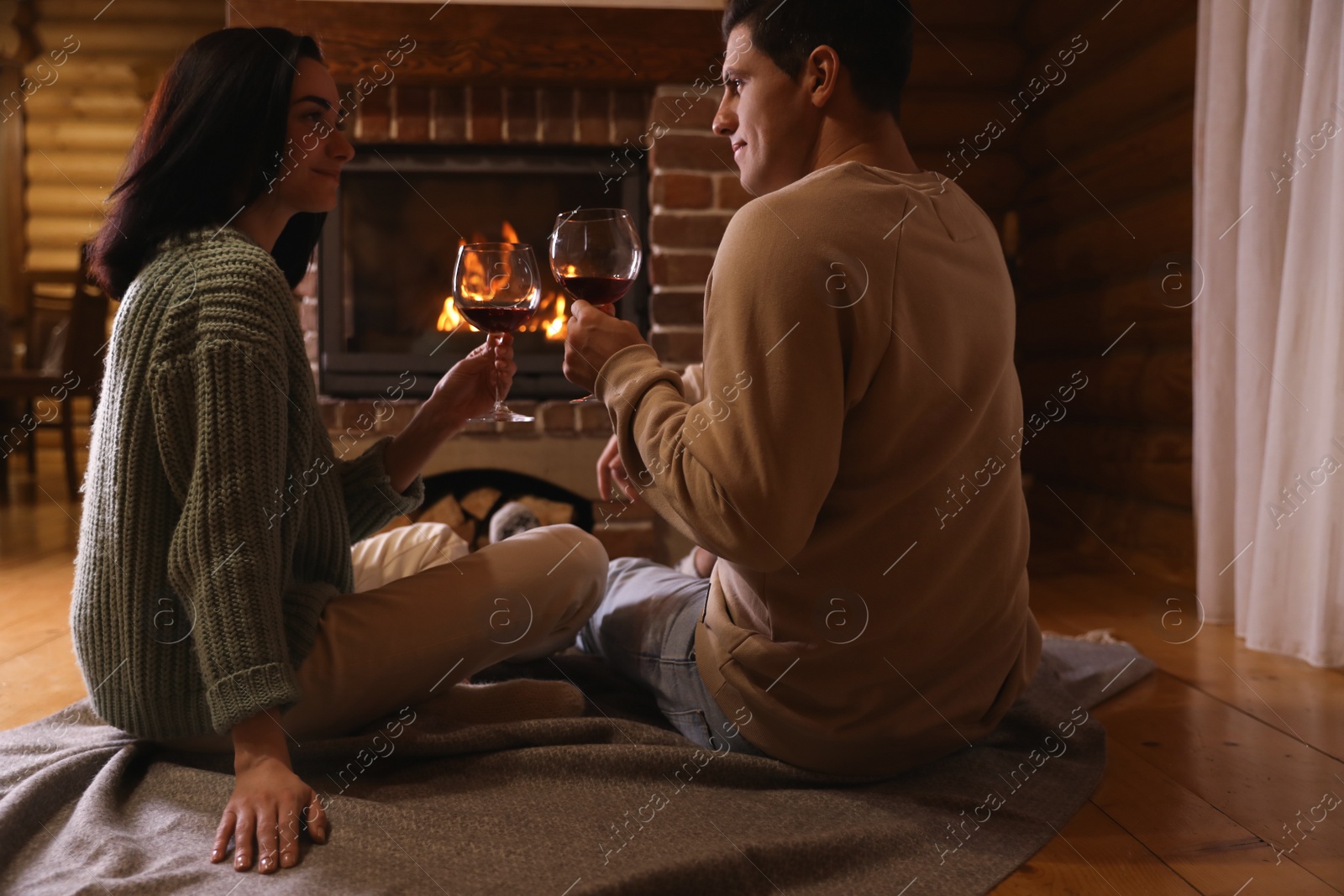 Photo of Lovely couple with glasses of wine near fireplace indoors. Winter vacation