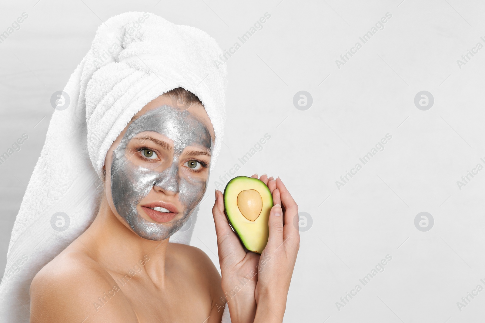 Photo of Beautiful woman holding avocado near her face with silver mask against light background. Space for text