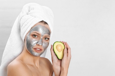 Photo of Beautiful woman holding avocado near her face with silver mask against light background. Space for text