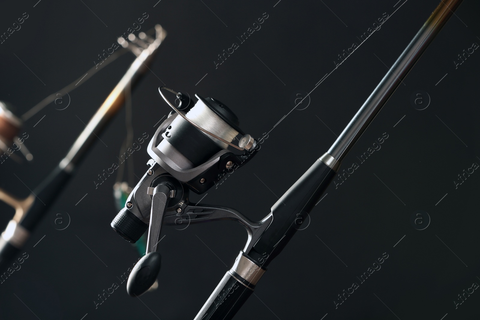 Photo of Modern spinning rod against dark background, closeup. Fishing equipment