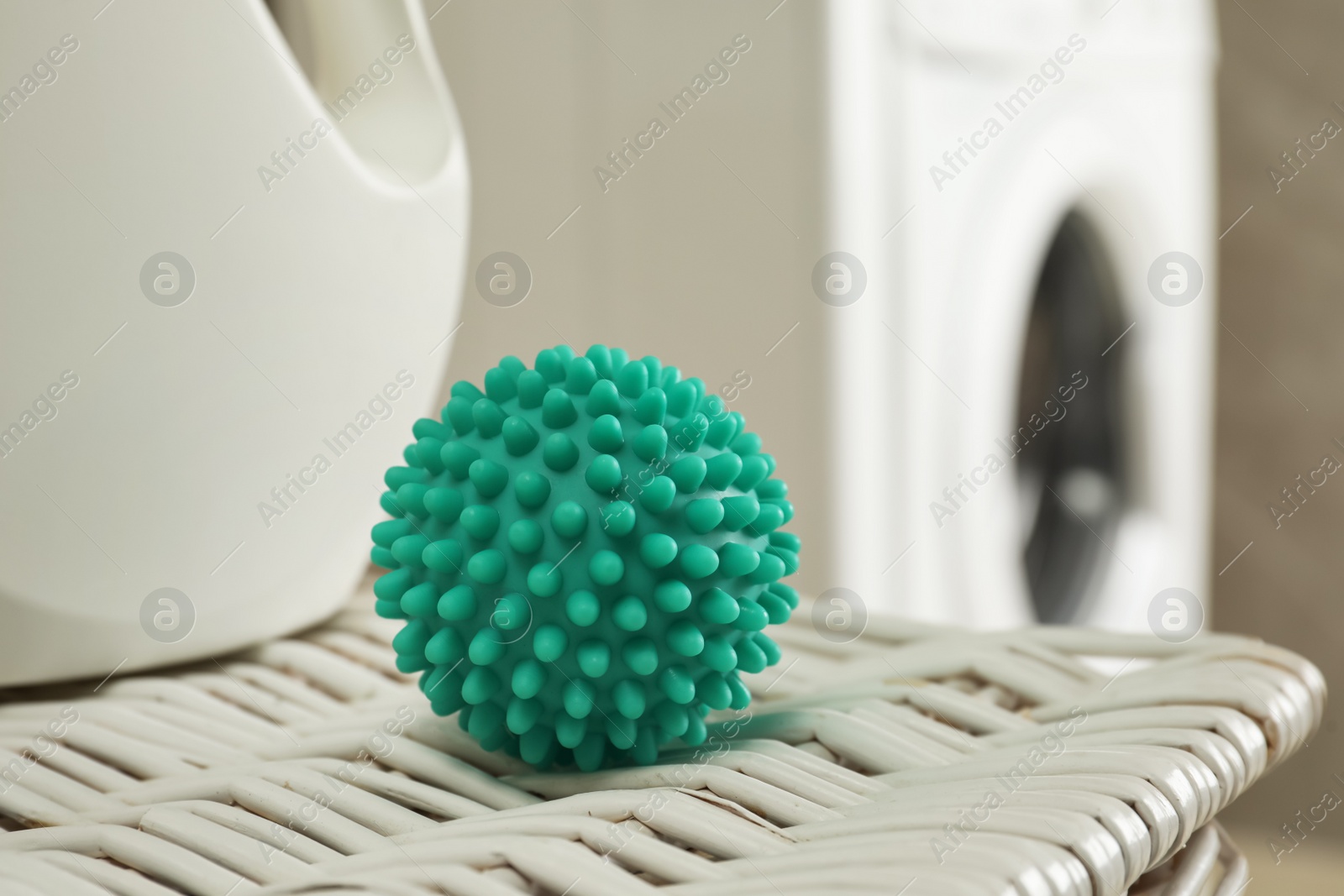 Photo of Turquoise dryer ball and laundry detergent on wicker basket near washing machine, closeup