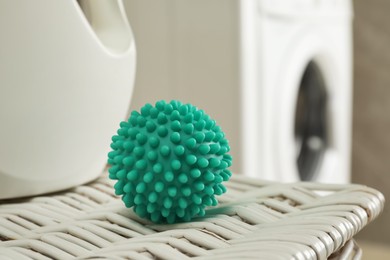Turquoise dryer ball and laundry detergent on wicker basket near washing machine, closeup
