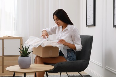 Photo of Happy young woman opening parcel at home. Internet shopping