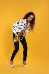 Beautiful African American woman playing saxophone on yellow background