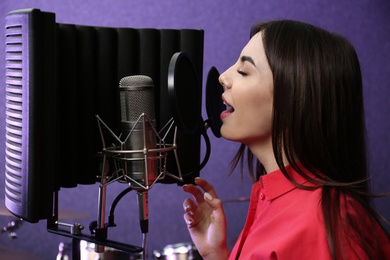 Photo of Young singer with microphone recording song in studio