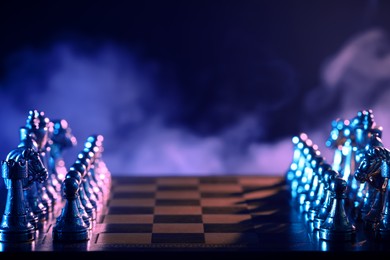Set of chess pieces on checkerboard in color light before game, selective focus. Space for text