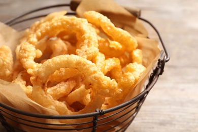 Photo of Homemade crunchy fried onion rings in wire basket on wooden background, closeup