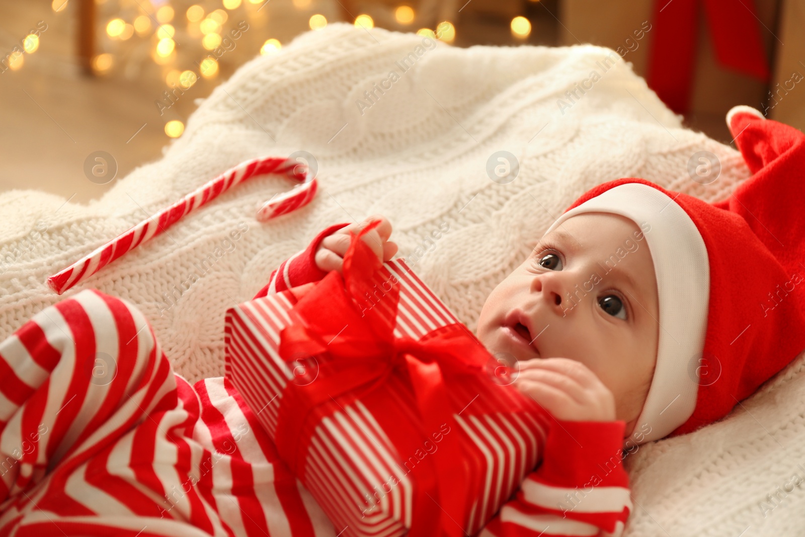 Photo of Cute little baby in Santa hat holding Christmas present on knitted blanket