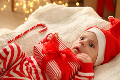 Photo of Cute little baby in Santa hat holding Christmas present on knitted blanket