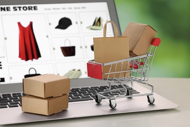 Photo of Mini shopping bag, boxes and cart on laptop, closeup. Online store