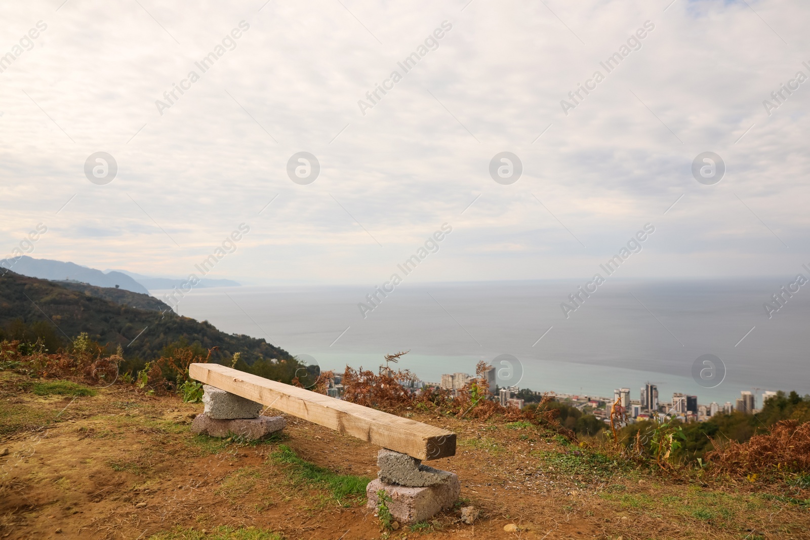 Photo of Picturesque view of city, beautiful sea and bench under cloudy sky