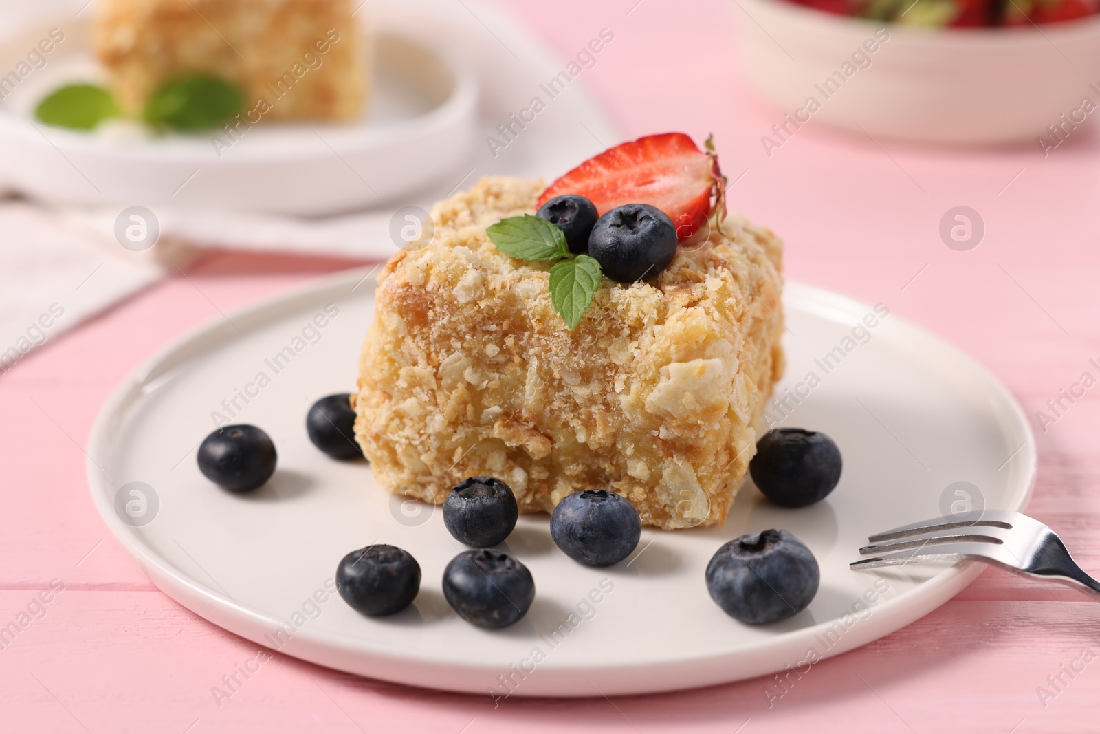 Photo of Piece of delicious Napoleon cake with fresh berries on pink wooden table, closeup