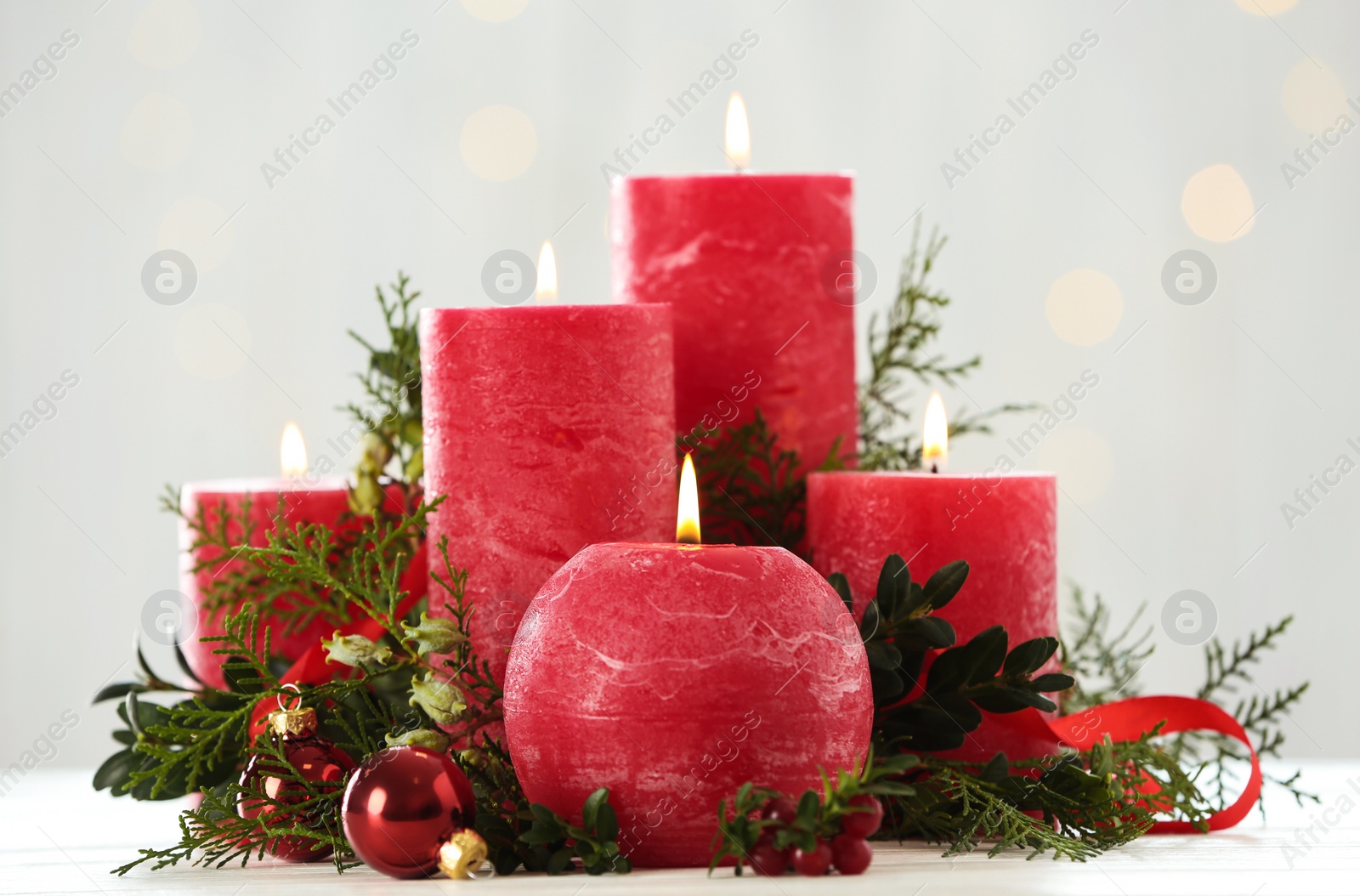 Photo of Burning red candles with Christmas decor on table against blurred lights