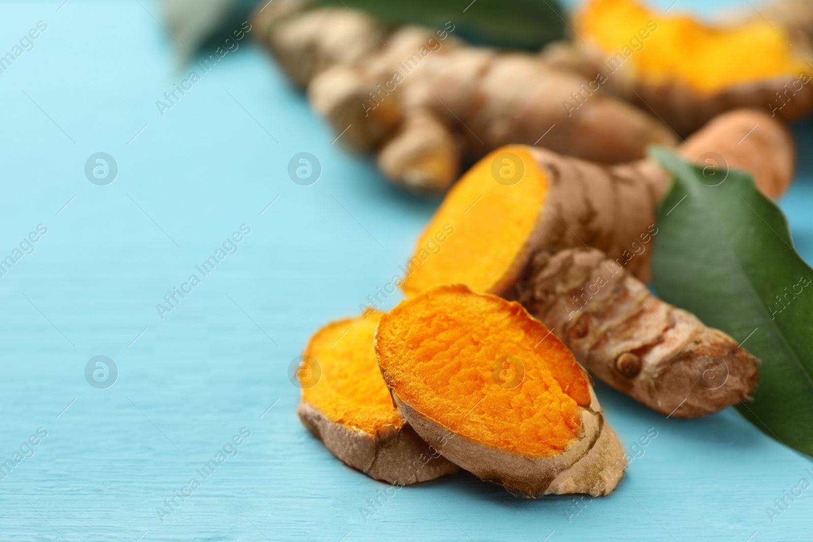 Photo of Cut turmeric roots on light blue wooden table, closeup. Space for text