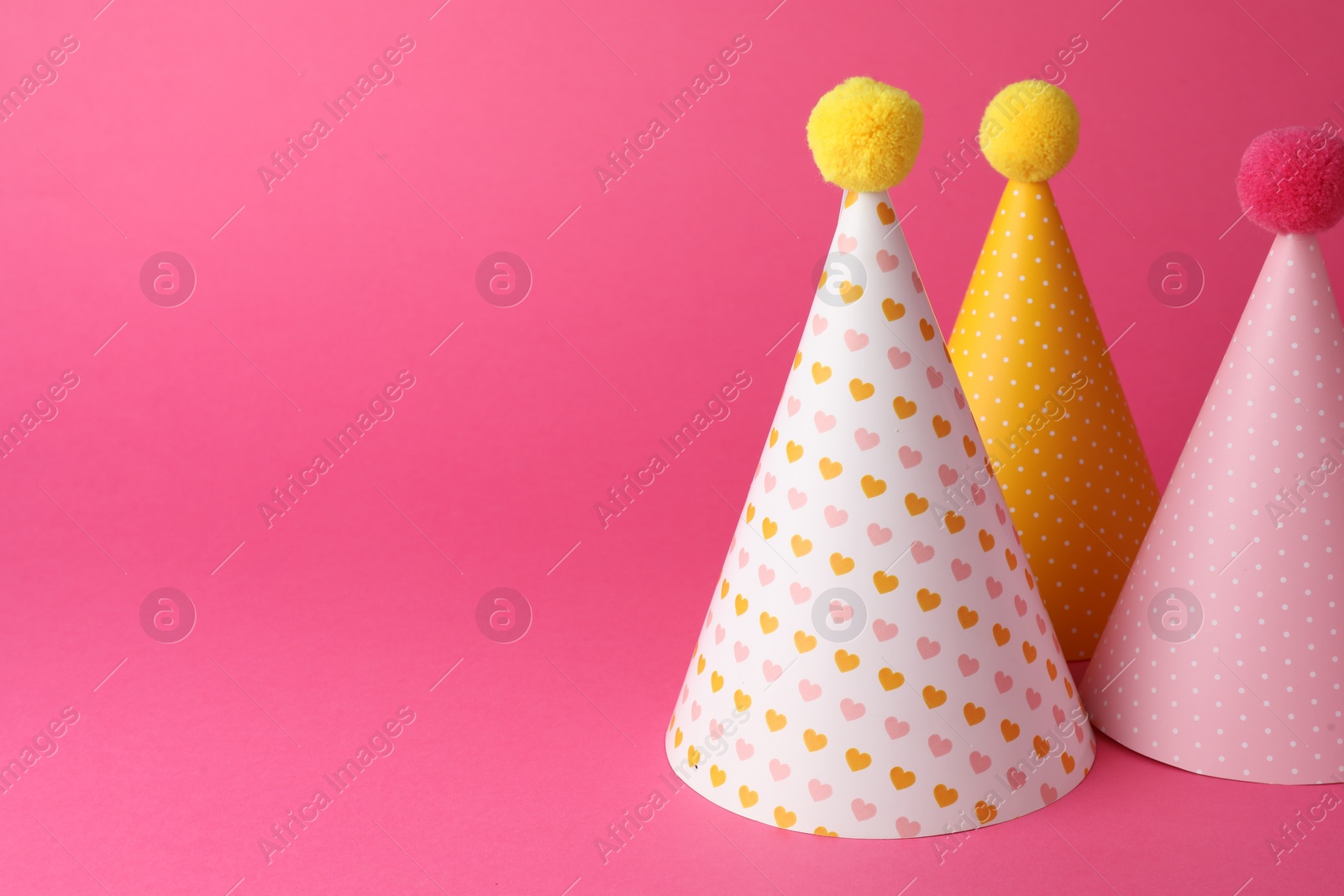 Photo of Beautiful party hats with pompoms on pink background, space for text