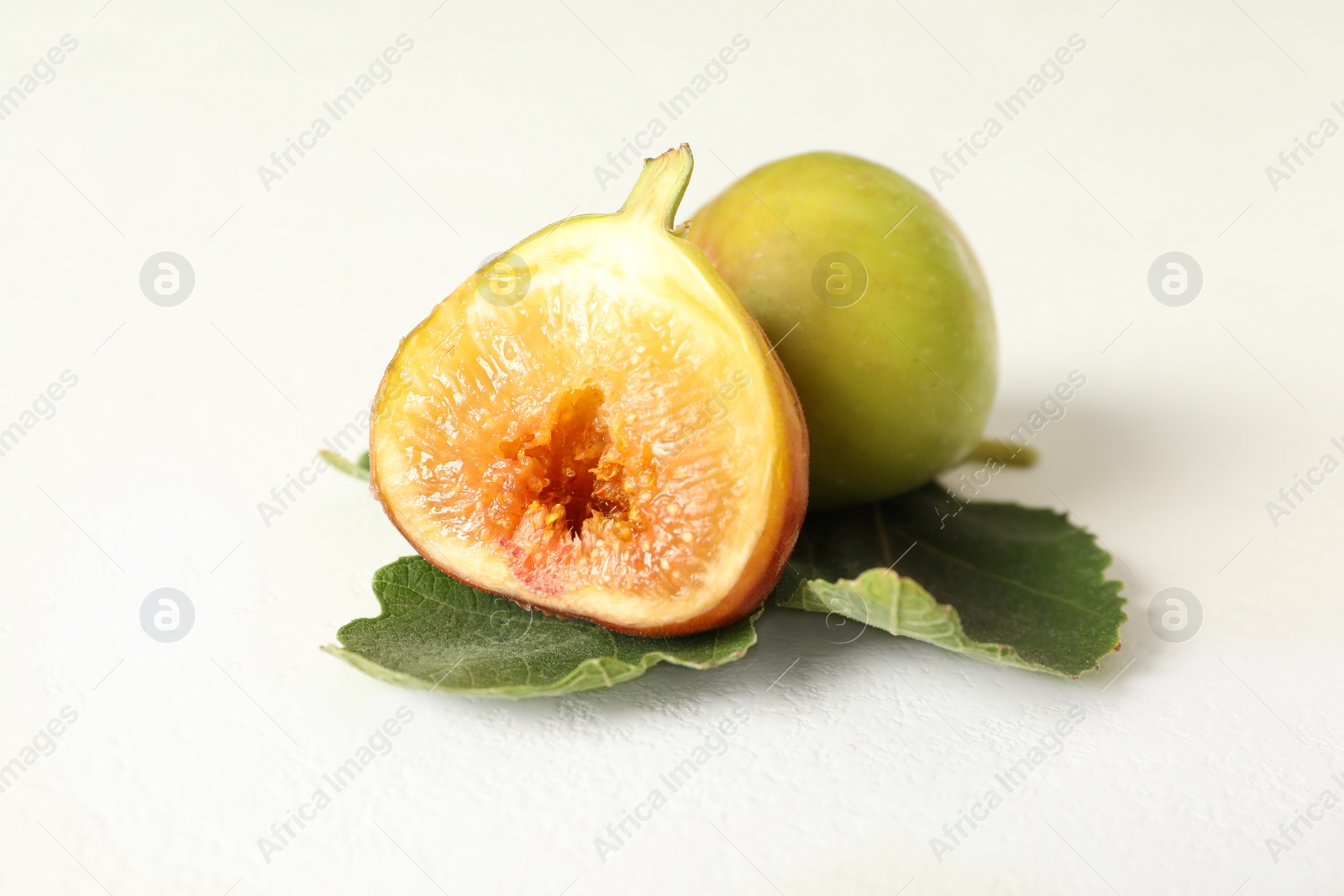 Photo of Whole and cut tasty fresh green figs with leaf on white table, closeup
