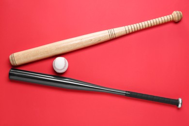 Photo of Baseball bats and ball on red background, flat lay