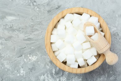 Photo of White sugar cubes in wooden bowl and scoop on grey table, top view. Space for text