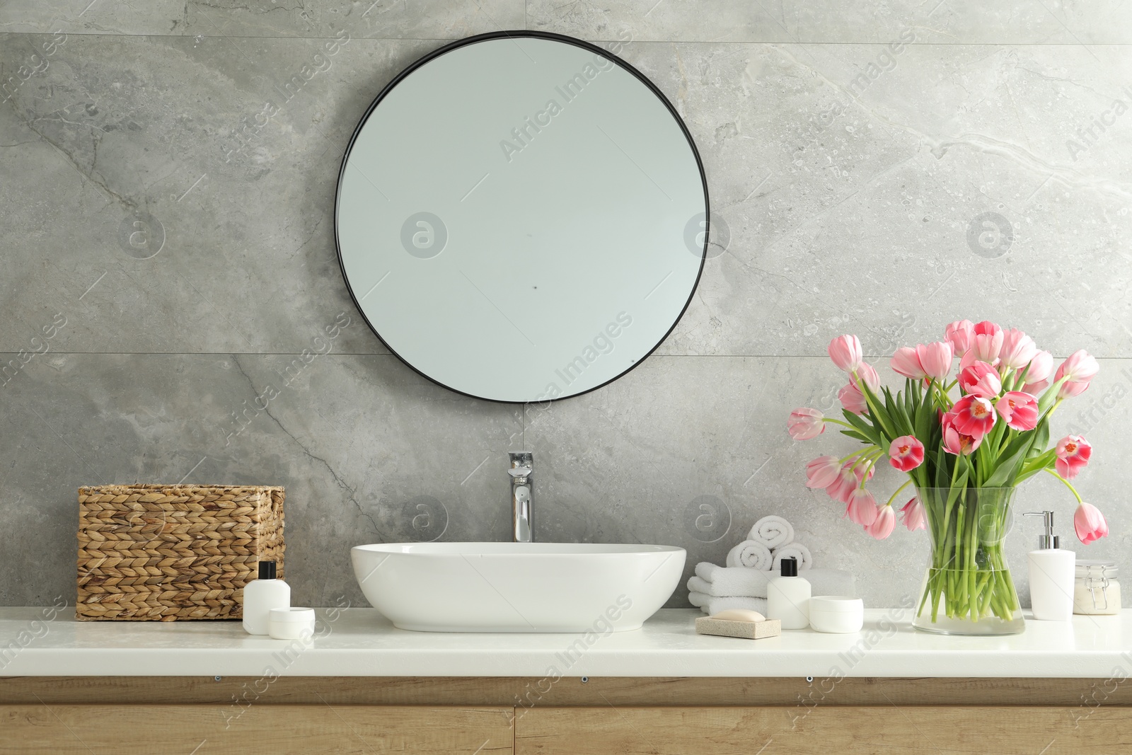 Photo of Vase with beautiful pink tulips and toiletries near sink in bathroom